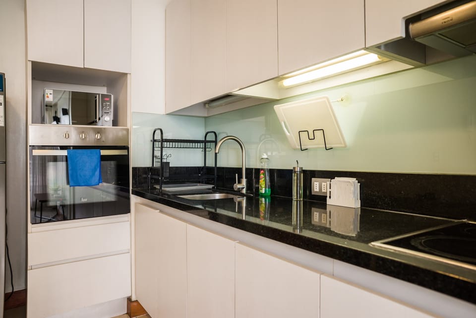 Private kitchen with sleek white cabinetry, black granite counters, modern appliances, and a tall curved faucet.