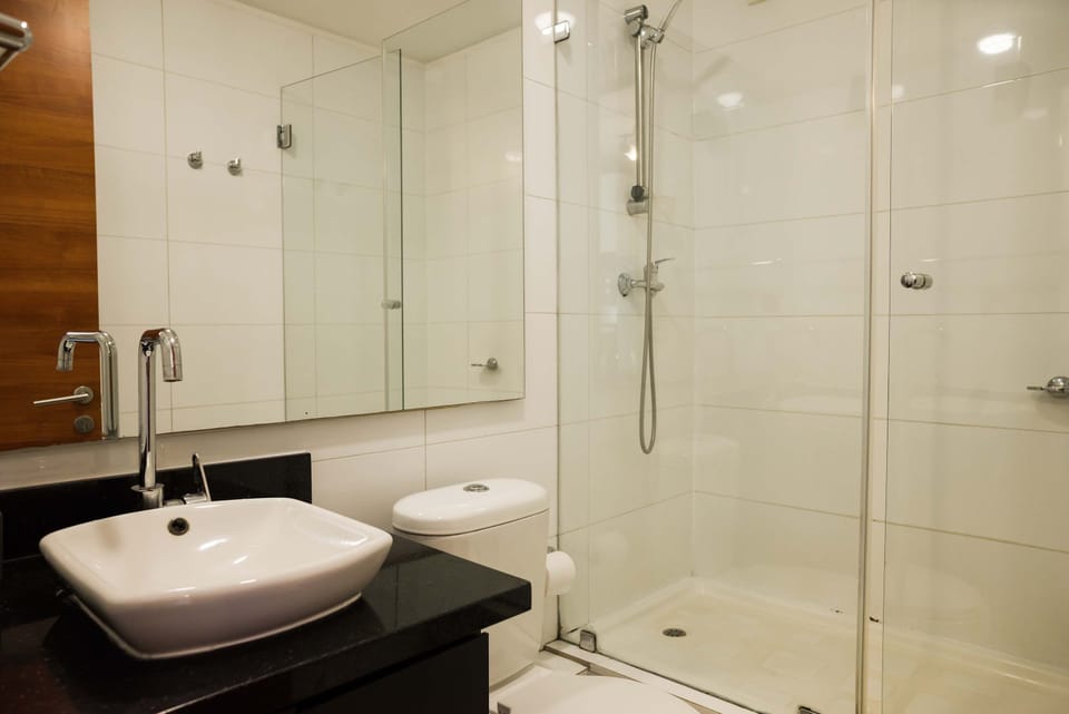 Private bathroom with a glass-enclosed walk-in shower, chrome handheld showerhead, vessel sink, mirrored cabinet, and black stone vanity.