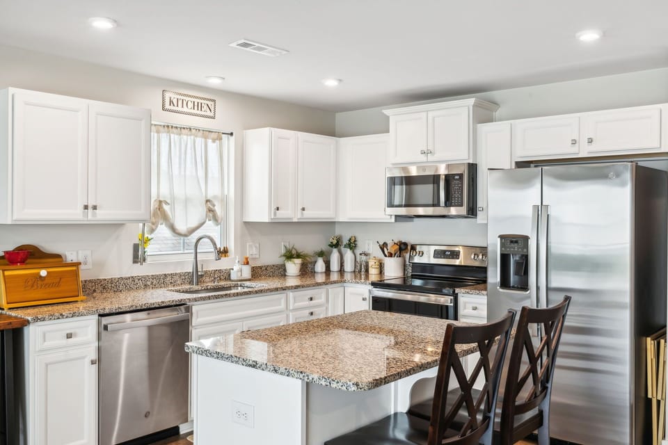 Modern kitchen with white cabinets, granite countertops, stainless steel appliances, and an island with two wooden chairs.