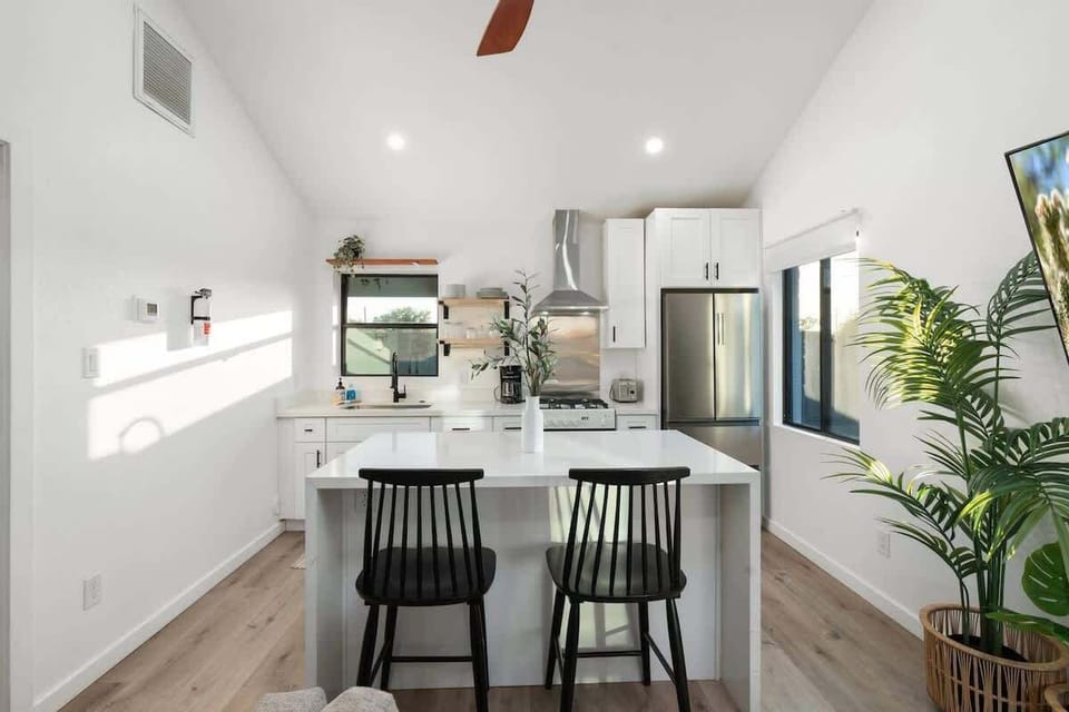 Cook and chat around the bright white kitchen—pull up to the island’s three black stools, prep on the counters, and keep the conversation flowing across the open layout with modern lighting overhead.