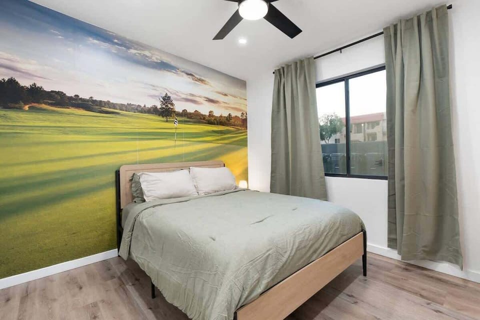 Queen bed with a bold golf-course mural and soft curtains—close the day out here, then wake up to natural light and a calm, uncluttered setup.