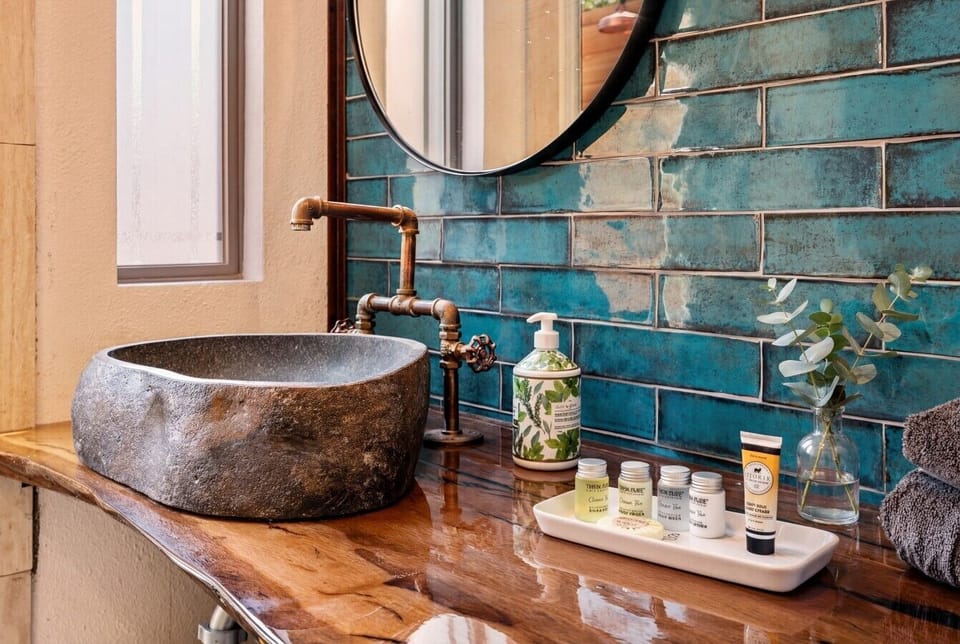 Stone vessel sink, copper pipe fixtures, and teal tile. Toiletries by Thena Pure included.