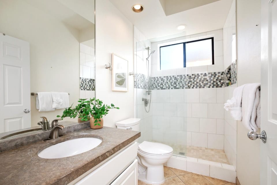 A crisp and modern guest bath featuring a stone vanity, glass walk-in shower, and mosaic tile accents for fresh appeal   