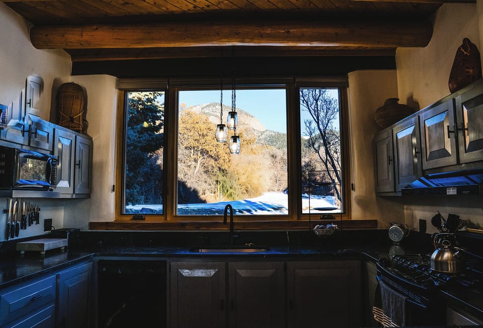 Cook your meals while gazing at snow-capped mountains through this rustic kitchen's panoramic window, where exposed beams create authentic charm.