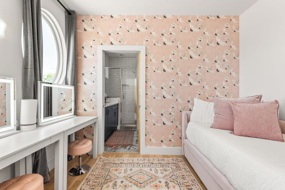 A cozy room featuring a daybed, patterned wallpaper, and natural light.
