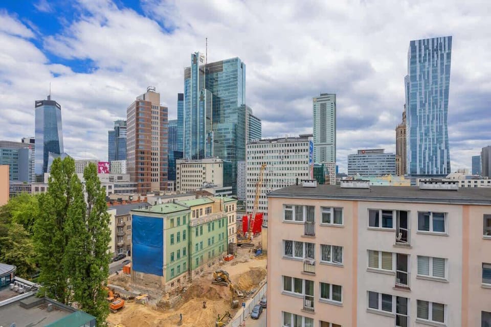 A city view from street level with a mix of old and new buildings, framed by trees.