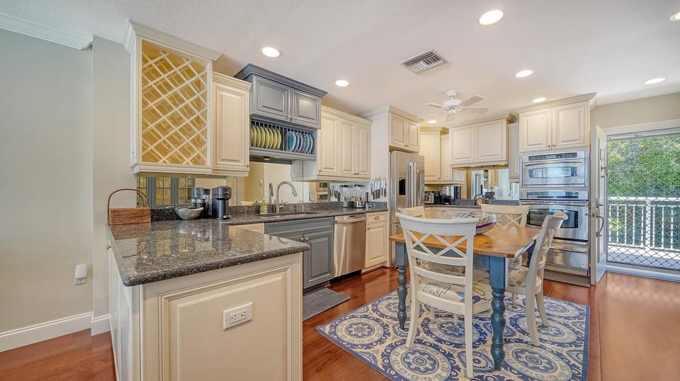 Kitchen with granite countertops, built-in wine rack, stainless steel appliances, and a blue patterned area rug under a wooden table.