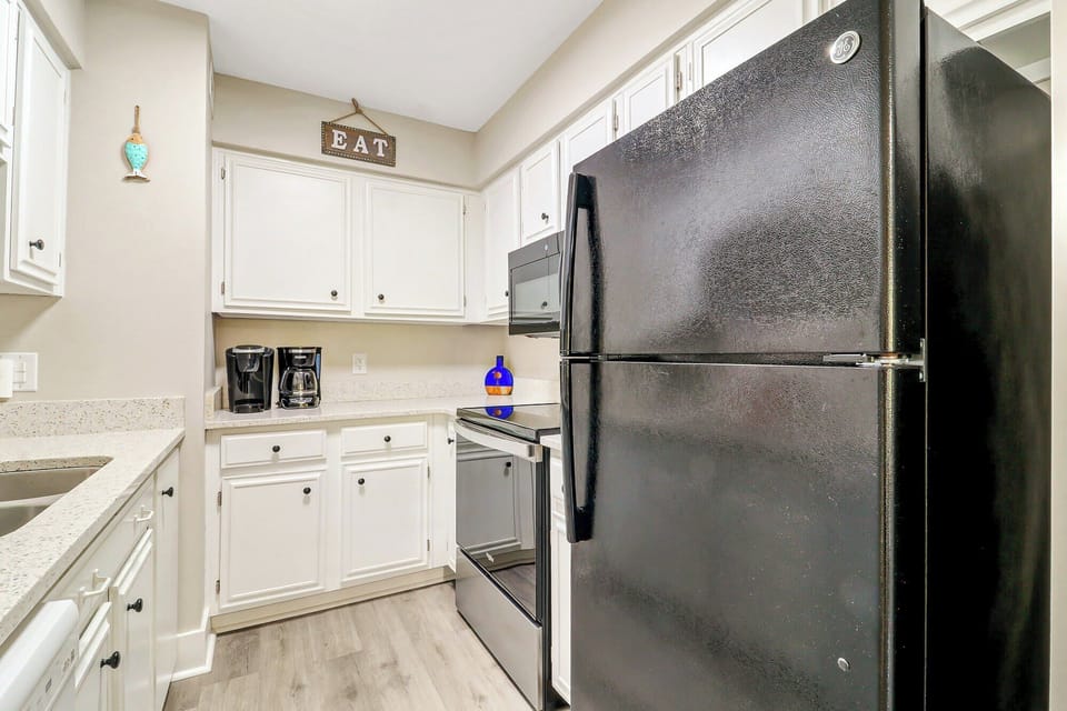 Creamy white cabinetry and speckled stone counters create a tidy, functional kitchen space for slow mornings. Soft overhead glow illuminates the coffee station and modern appliances, making every meal prep a breeze.