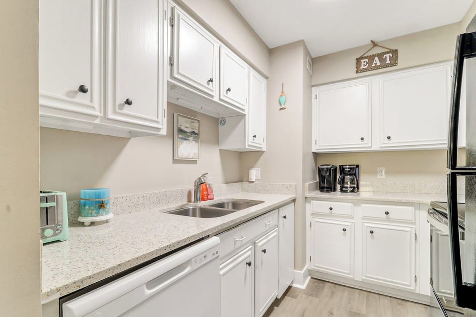 Bright white cabinetry and stone counters create a crisp, airy kitchen ready for slow mornings. A dedicated coffee station and soft, creamy walls offer a calm space to prep your favorite beachside snacks.