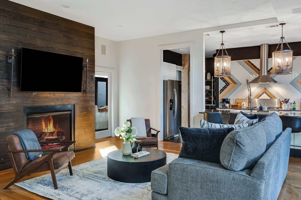 Gather in the stylish main living area featuring a cozy gas fireplace, rich wood accent wall, and plush seating—perfect for relaxing after a day exploring Nashville.