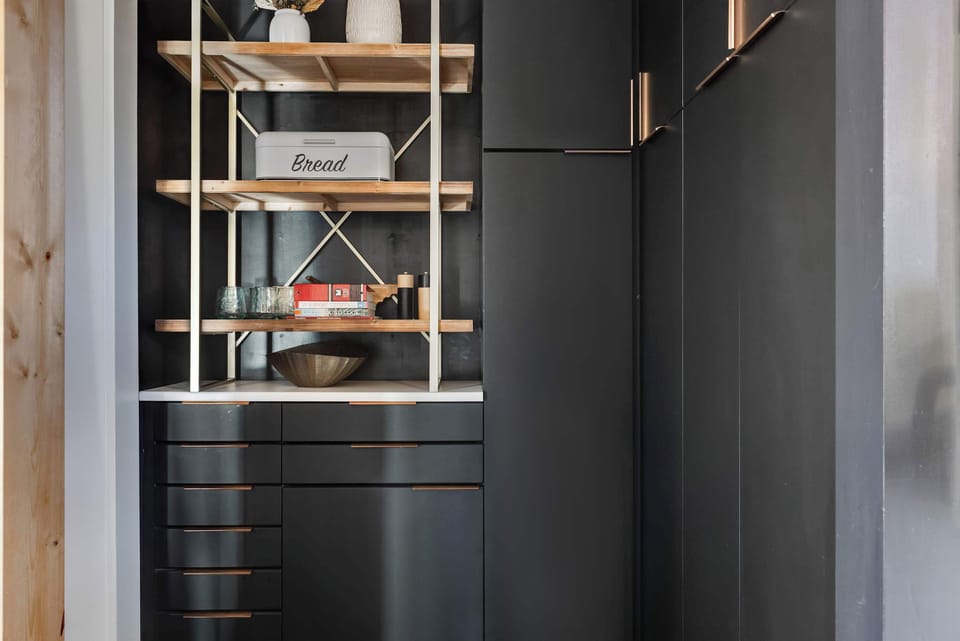 A sleek pantry with modern cabinetry and open wood shelving provides plenty of storage, blending function with beautiful design accents.