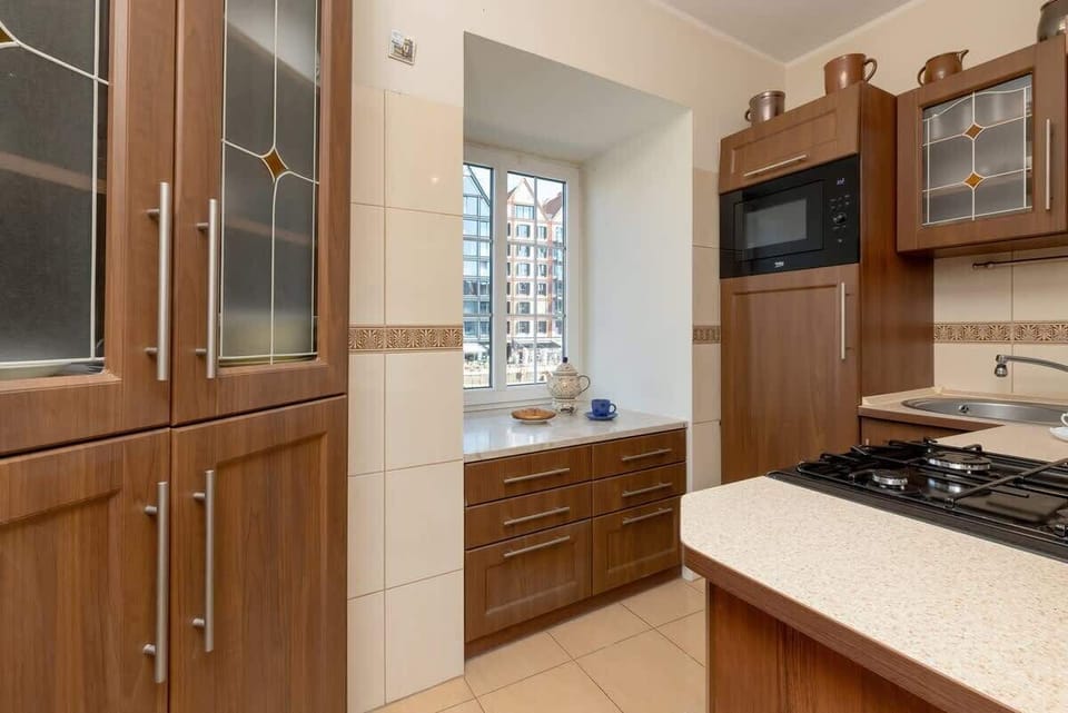 A wider view of the kitchen with a gas stove, oven, and upper cabinets with glass fronts. The combination of natural wood and light walls is traditional yet clean.
