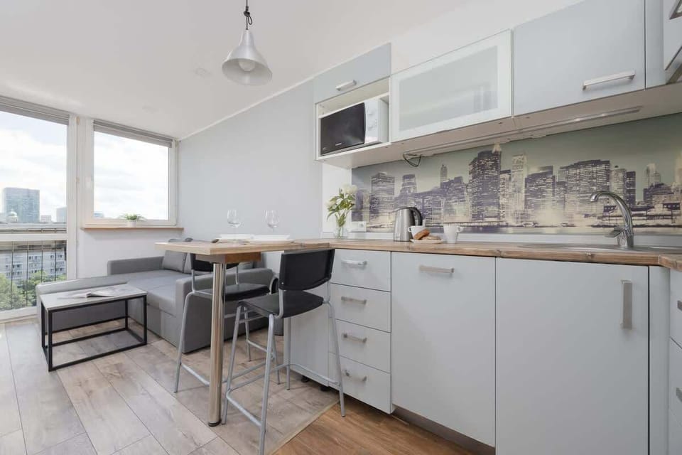 A small, modern kitchen with a white and gray color palette, tile backsplash, and wood flooring.