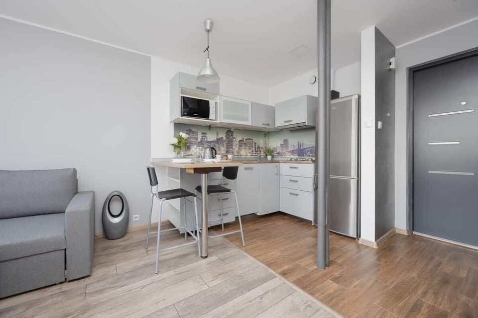 A kitchen area leading into a hallway, showing the fridge, and gray couch in the corner.
