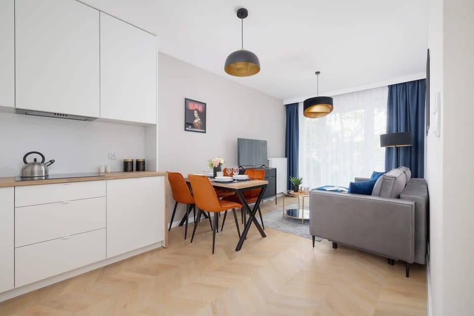 A spacious living and dining area with light wood finishes, orange chairs, and elegant lighting.