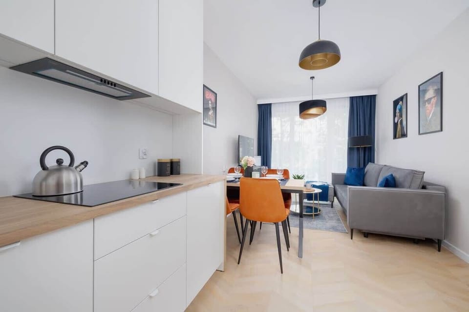 A living space with a mounted television, modern sofa, and adjacent dining area with orange chairs..
