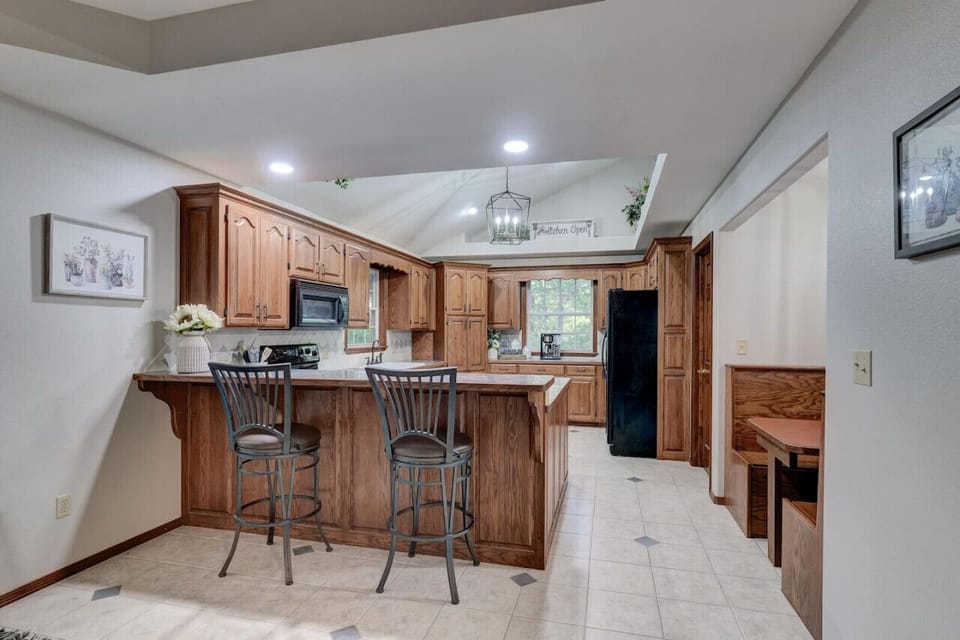 Cozy kitchen setup with a wooden diner-style table and seating, a high table with a classic high chair, stylish built-in wooden cabinets, kitchen appliances, and a petite glass window.