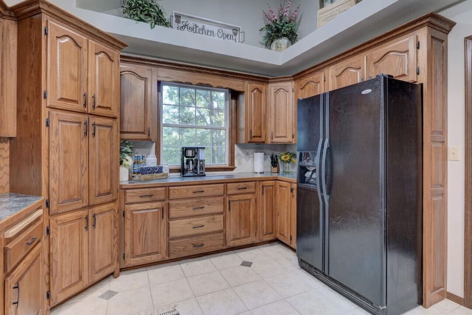 Functional kitchen space showcasing extensive wooden cabinetry, a fridge, coffee essentials neatly arranged, and a sunny window