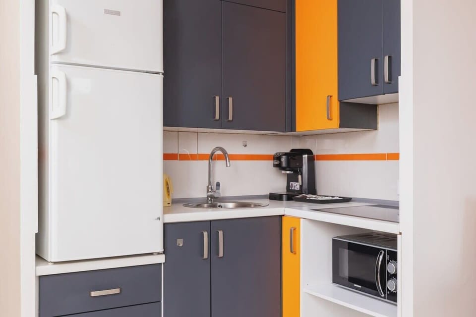 A functional kitchen space with bold orange and grey cabinetry, next to a dining set, ideal for modern living.