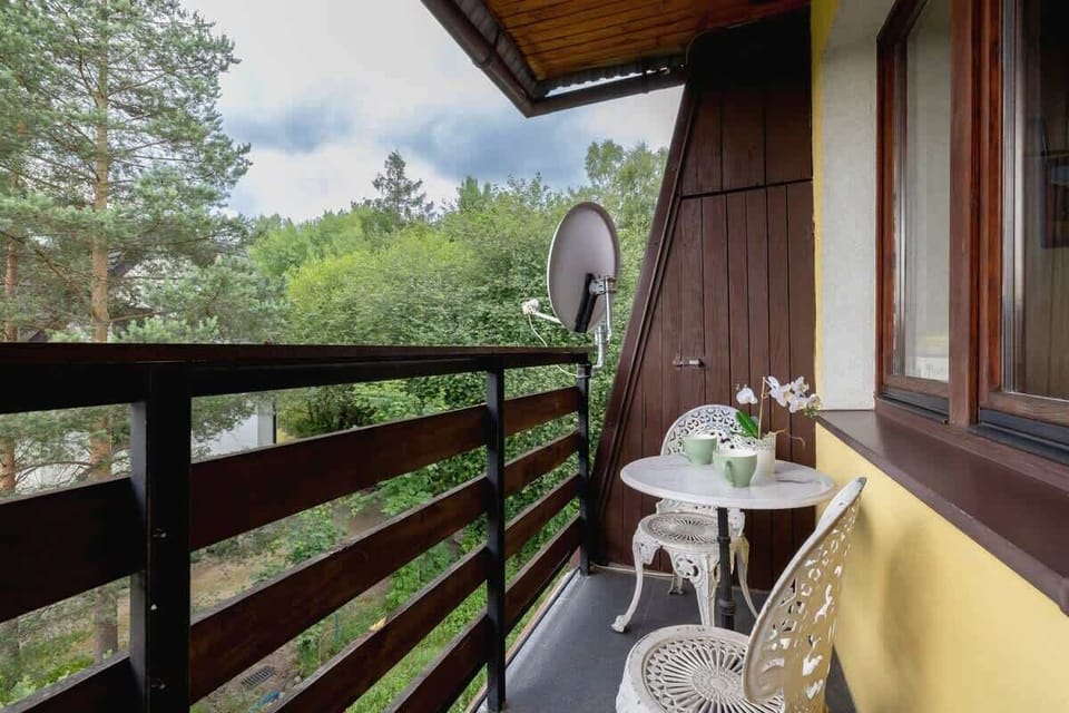 A shaded balcony overlooking a forested area and rolling hills, with wooden railings and minimal furniture for relaxation.