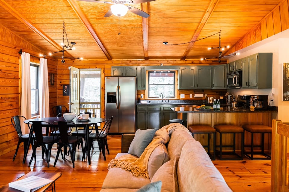 An open-concept living space with a cozy wood-paneled ceiling, a comfortable sofa, a dining table, and a fully-equipped kitchen