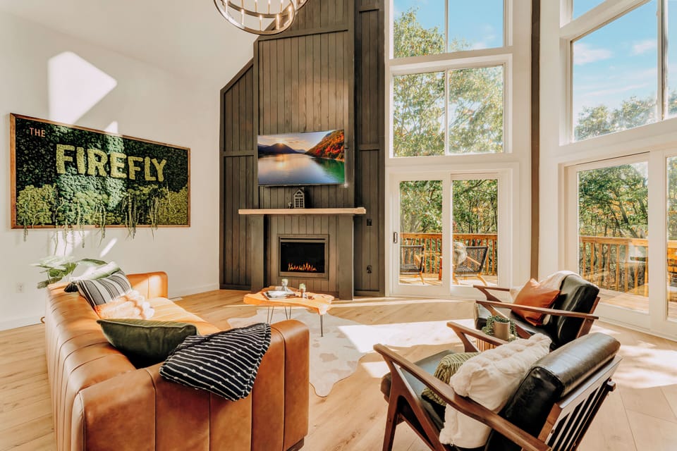 Primary Living room with large Smart TV and propane fireplace. Soak up the sun with gorgeous extra large A-frame windows.  Learn more about our guest experience at truenorthpocono.com!