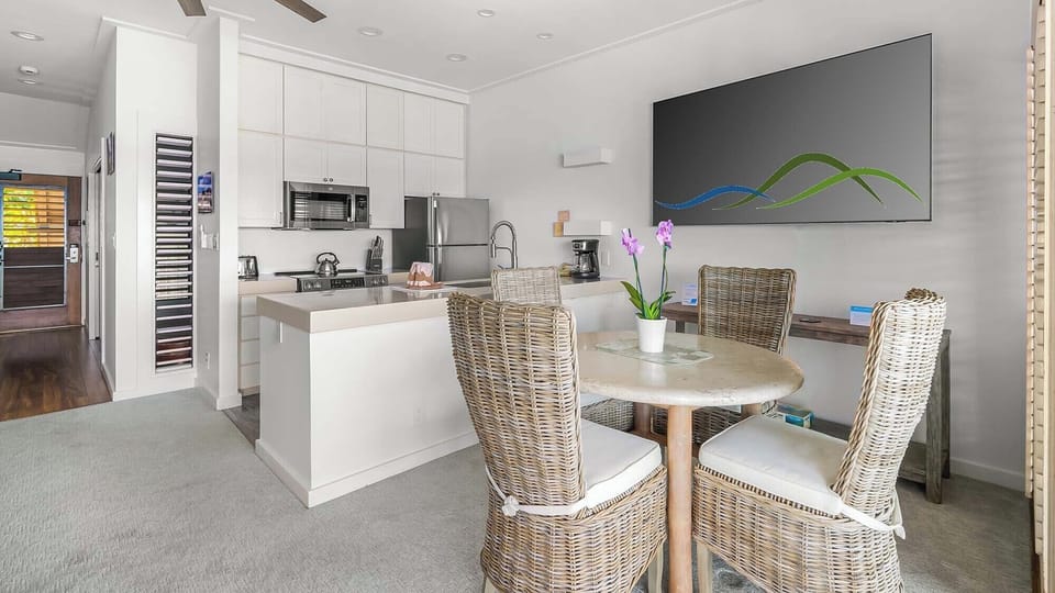 Picture yourself preparing meals in this sleek, modern kitchen, complete with stainless steel appliances and ample counter space. Dine at the cozy table for four, surrounded by coastal-inspired wicker chairs and natural light.