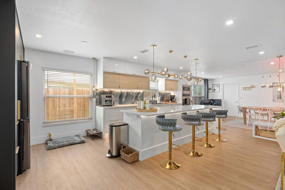 Open-concept kitchen with white cabinets, large marble island, bar stools and globe pendant lights, Bird House Spa Winter Park