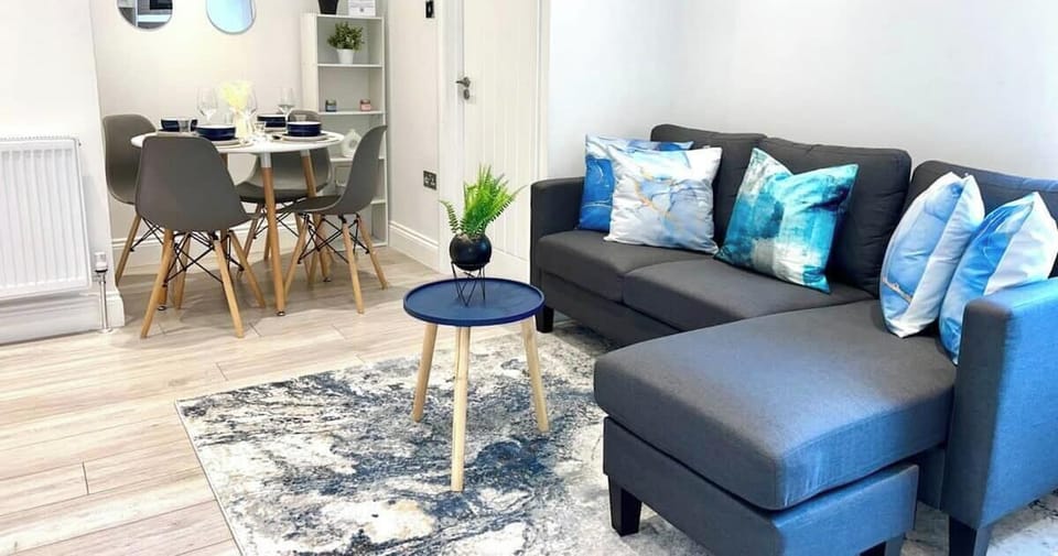 Modern lounge and dining area featuring a comfy sectional sofa, stylish dining table for four, contemporary décor, bright lighting, soft rug, and a welcoming open-plan layout ideal for relaxing or entertaining