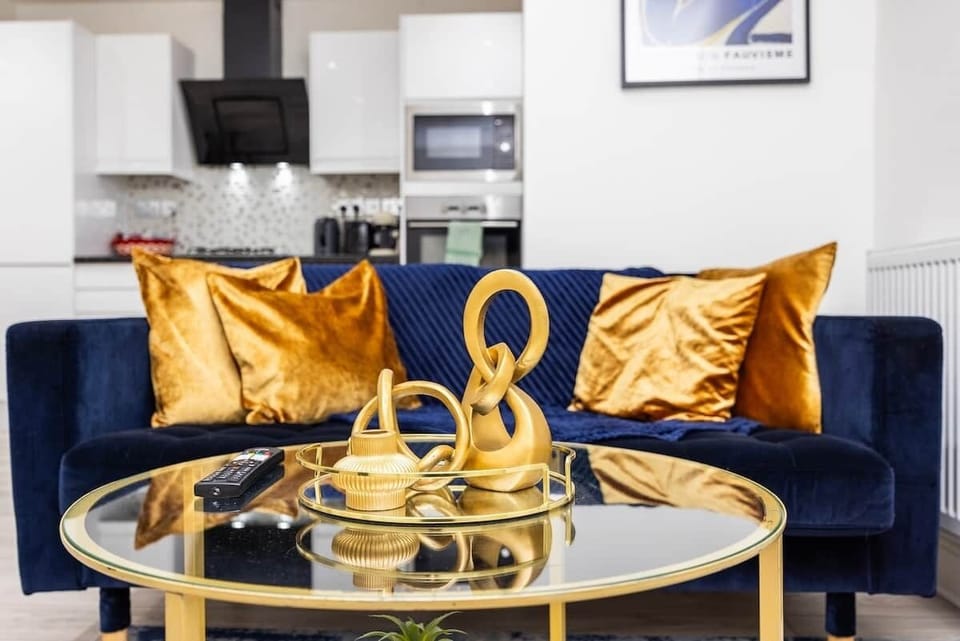 This stylish open-plan lounge features a charcoal sofa and a blue velvet sofa, perfect for groups. With chic gold accents and a designer rug, it’s a bright, modern space to relax.