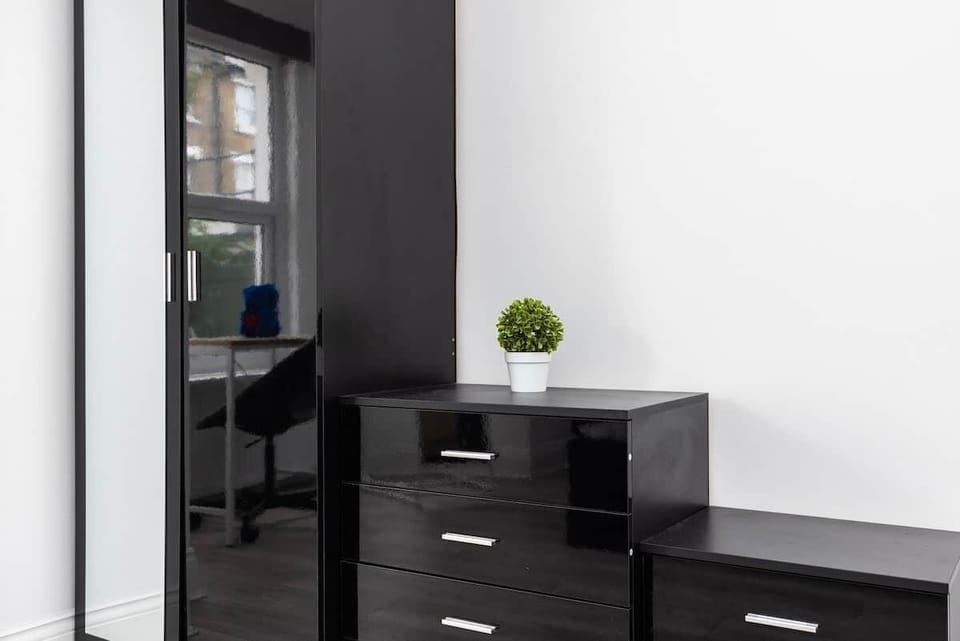 Spacious bedroom equipped with a double bed, dedicated workspace by the window, and full-length mirror. The room offers ample storage with bedside tables and a large wardrobe, all set within a bright, recessed-lit interior.