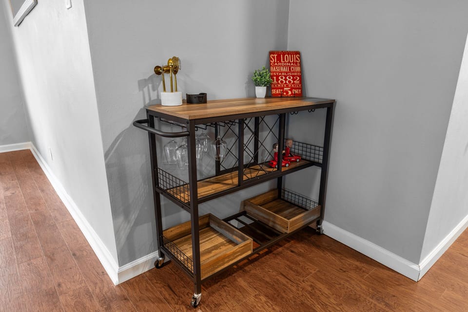 Rolling wood-and-metal serving cart with glassware, trays, bottle storage, and St. Louis decor.