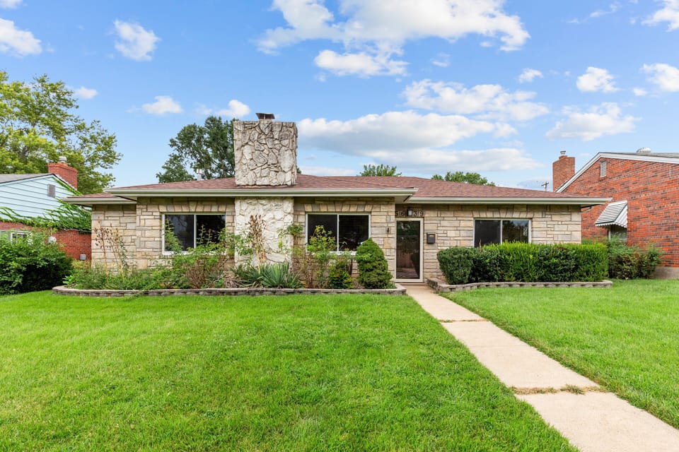 Front view of the single-story stone-faced home, lawn, walkway, and central entrance.
