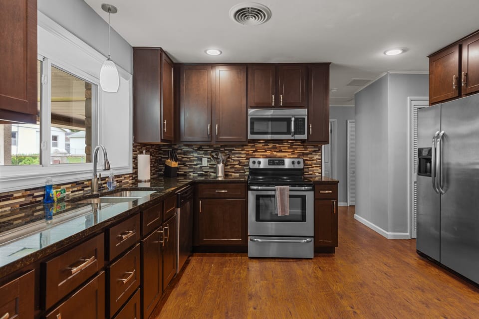 Full kitchen with dark wood cabinets, stainless-steel appliances, stone counters, and a mosaic backsplash.