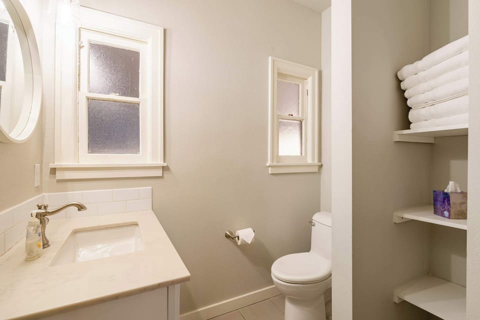 Bathroom vanity and toilet beside open towel storage.