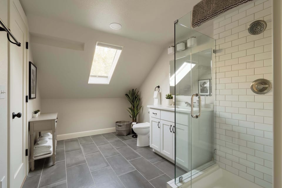 Bathroom with glass-enclosed walk-in shower, vanity, toilet and skylight.