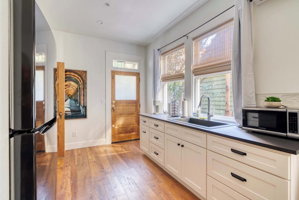 Counter space along the windows with a built-in sink, ample cabinetry, and a microwave beside the refrigerator.