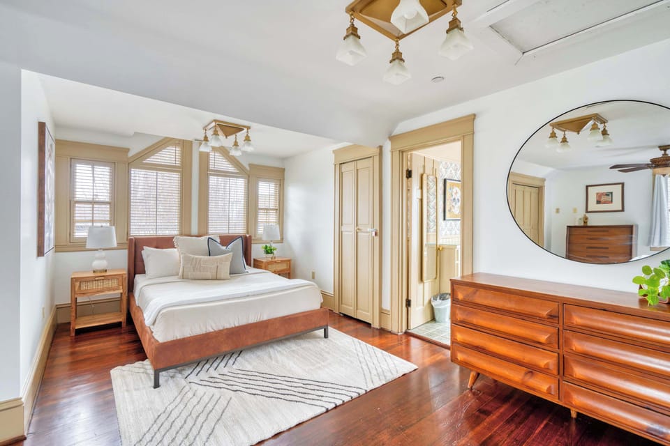 Bedroom with a wood bed frame, dresser and curtained windows.