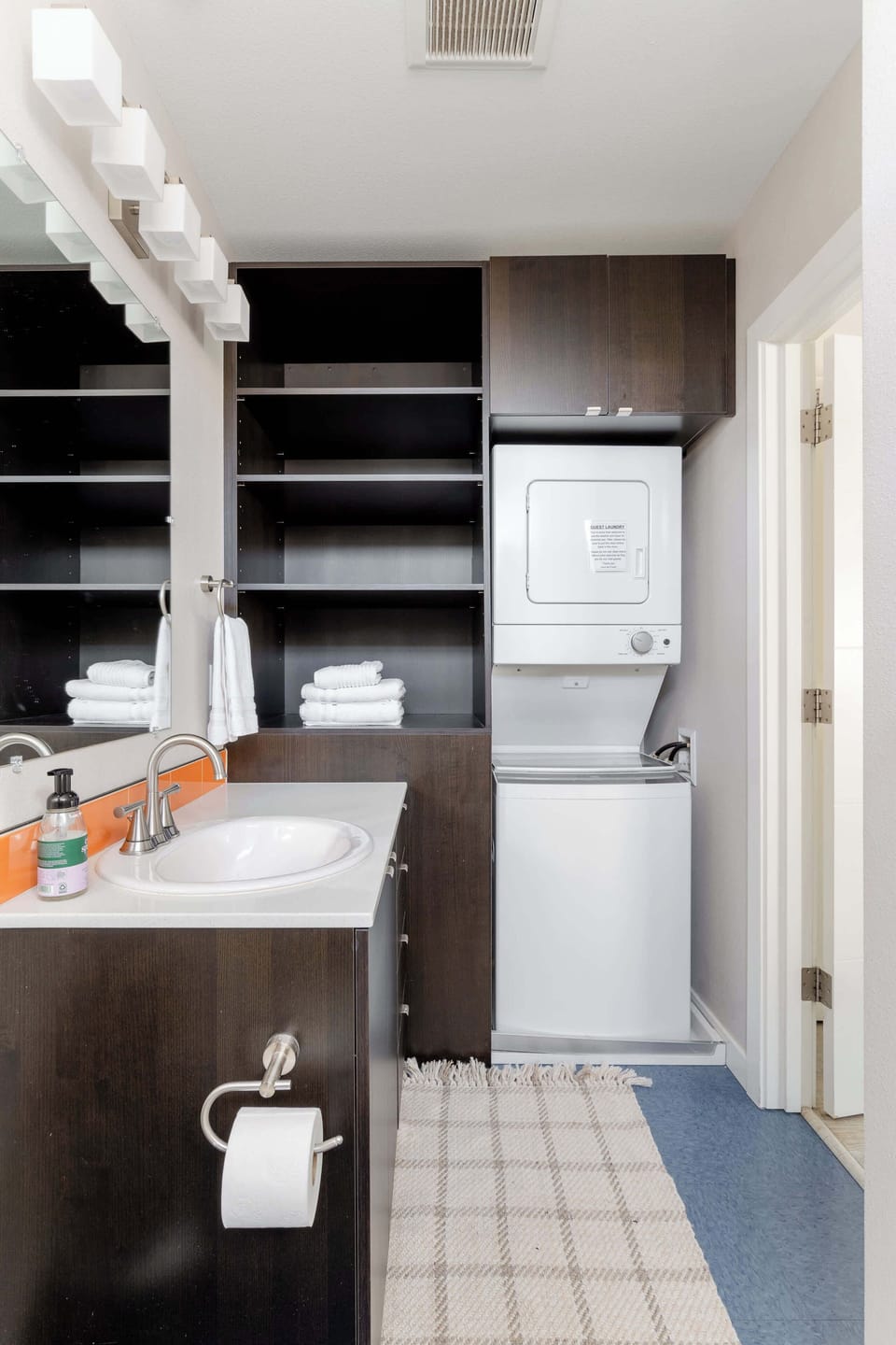 Bathroom with stacked washer and dryer beside open shelves.