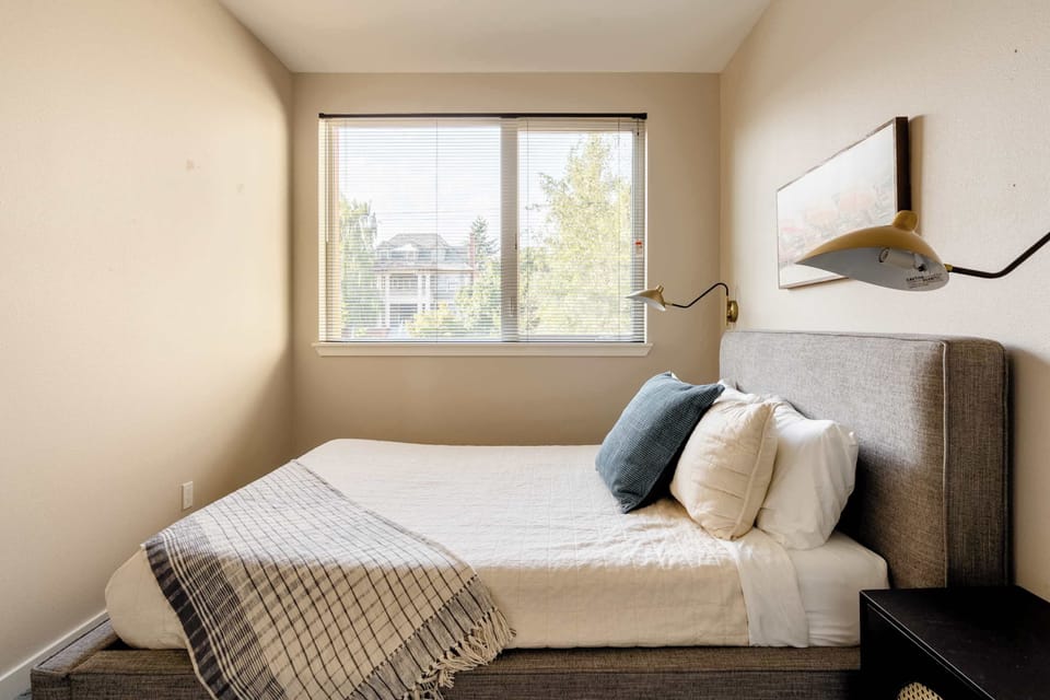 Upholstered bed beside a window and wall-mounted bedside lamps.