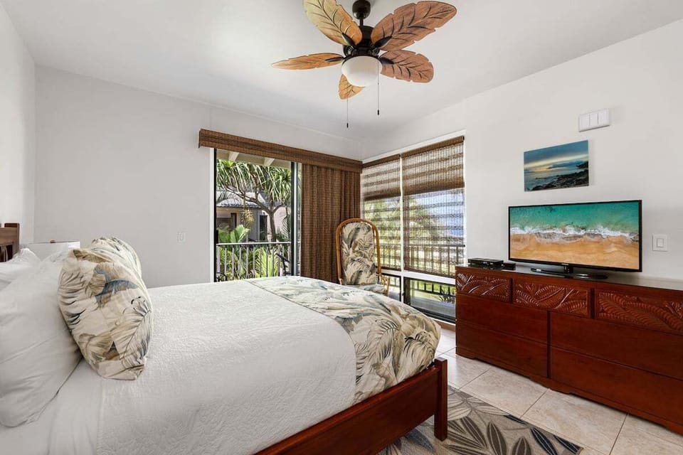 Peaceful bedroom with a king bed, ceiling fan, wood furnishings, and sliding doors opening to lush garden and partial outdoor views.