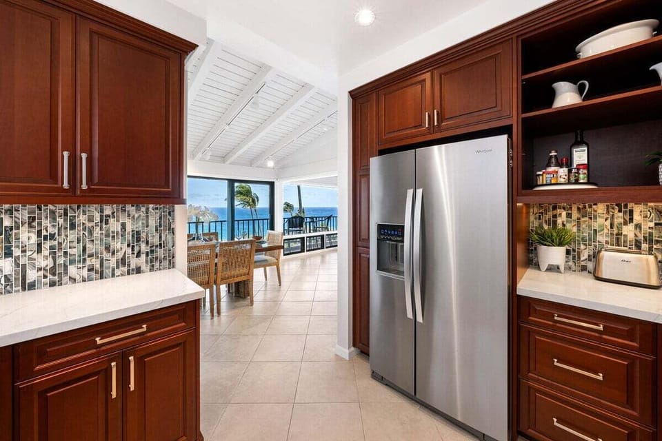 Well-appointed kitchen featuring granite countertops, stainless steel refrigerator, rich wood cabinetry, and convenient access to the dining area.