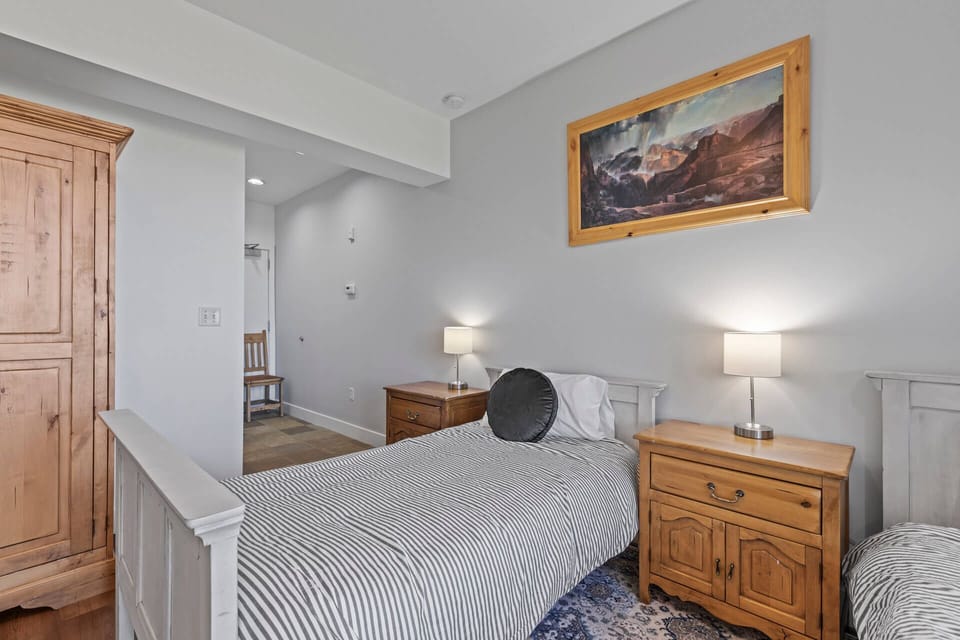 Unwind in this peaceful bedroom with its soft lighting, cozy bedding, and charming mountain artwork setting a tranquil, home-away-from-home atmosphere for your restful nights.