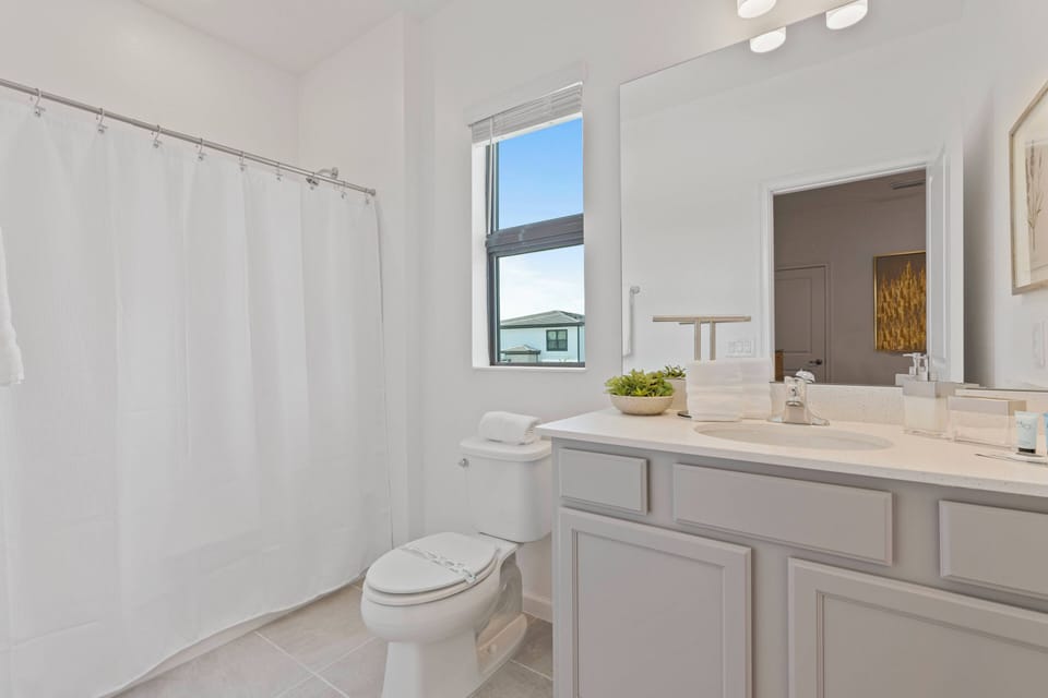 This bright bathroom features a sleek white design that enhances natural light. The modern vanity offers generous counter space and stylish fixtures, ensuring both functionality and sophistication for your comfort.