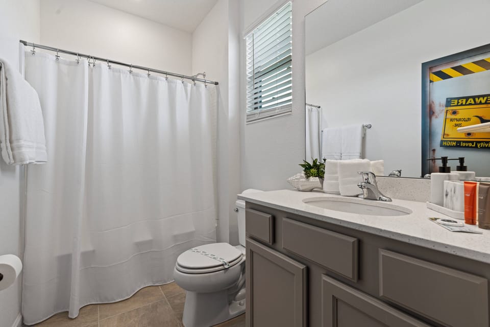This bright bathroom features a sleek granite countertop paired with soft gray cabinetry, offering a clean and refined look. The large window allows natural light to flood the space, while decorative accents add a touch of charm.