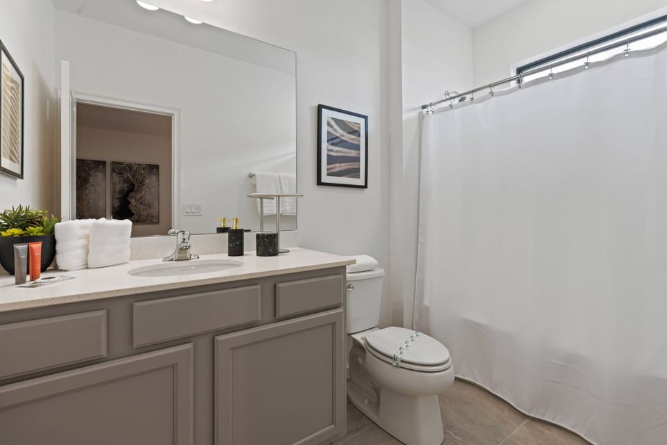 Experience a stylish bathroom with a modern gray vanity and a spacious mirror that brightens the space. The white shower curtain and neatly arranged fresh towels create an inviting, minimalist atmosphere for your comfort.