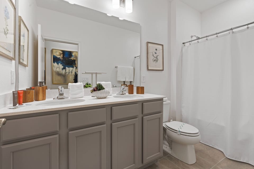 Welcome to this beautifully designed bathroom, where a sleek, light-colored vanity enhances the warm decor. The large mirror creates a bright atmosphere, and tasteful artwork adds a charming touch to your experience.