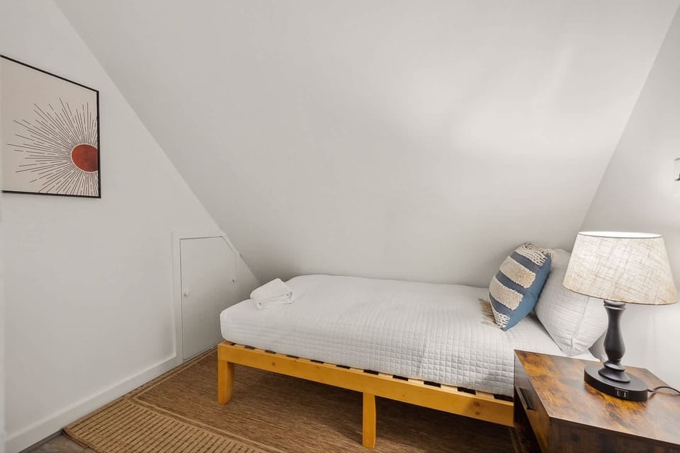 Cozy single bed with a wooden frame and soft lighting in a compact attic room.
