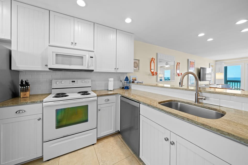 Your fully equipped kitchen features granite counters, modern appliances, and ocean views through the open living area.