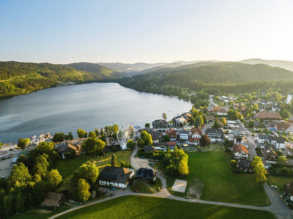 View on lake Titisee surrounded by green hills & forest.
